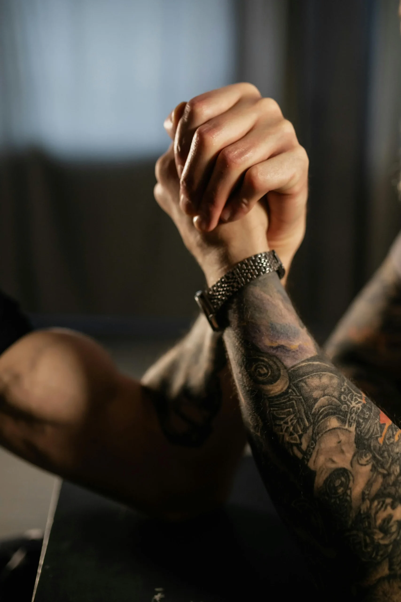 Two tattooed men holding hands, showcasing their connection and affection in a warm, intimate moment.