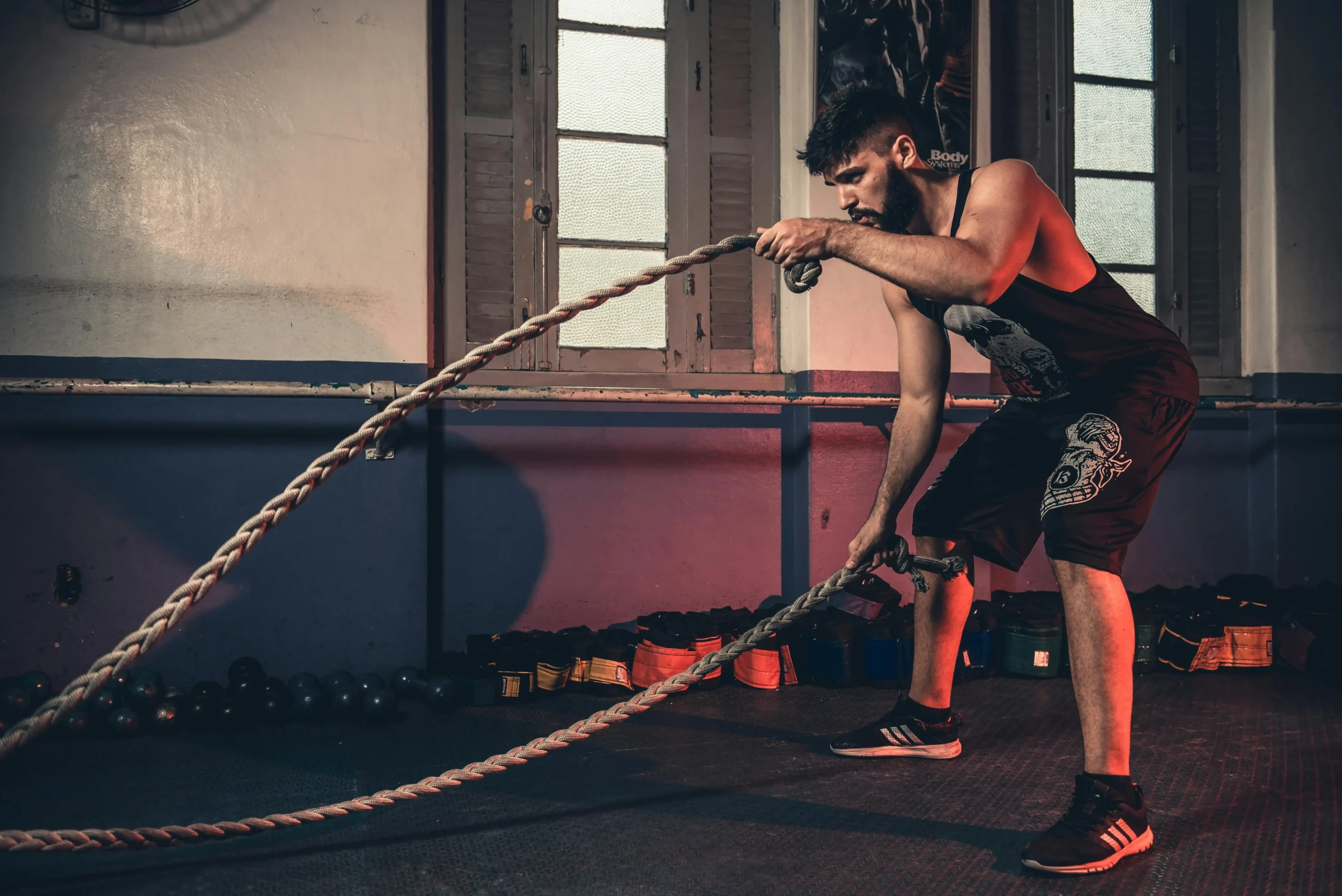 . In a gym setting, a man is engaged in a strength training exercise, pulling a heavy rope.
